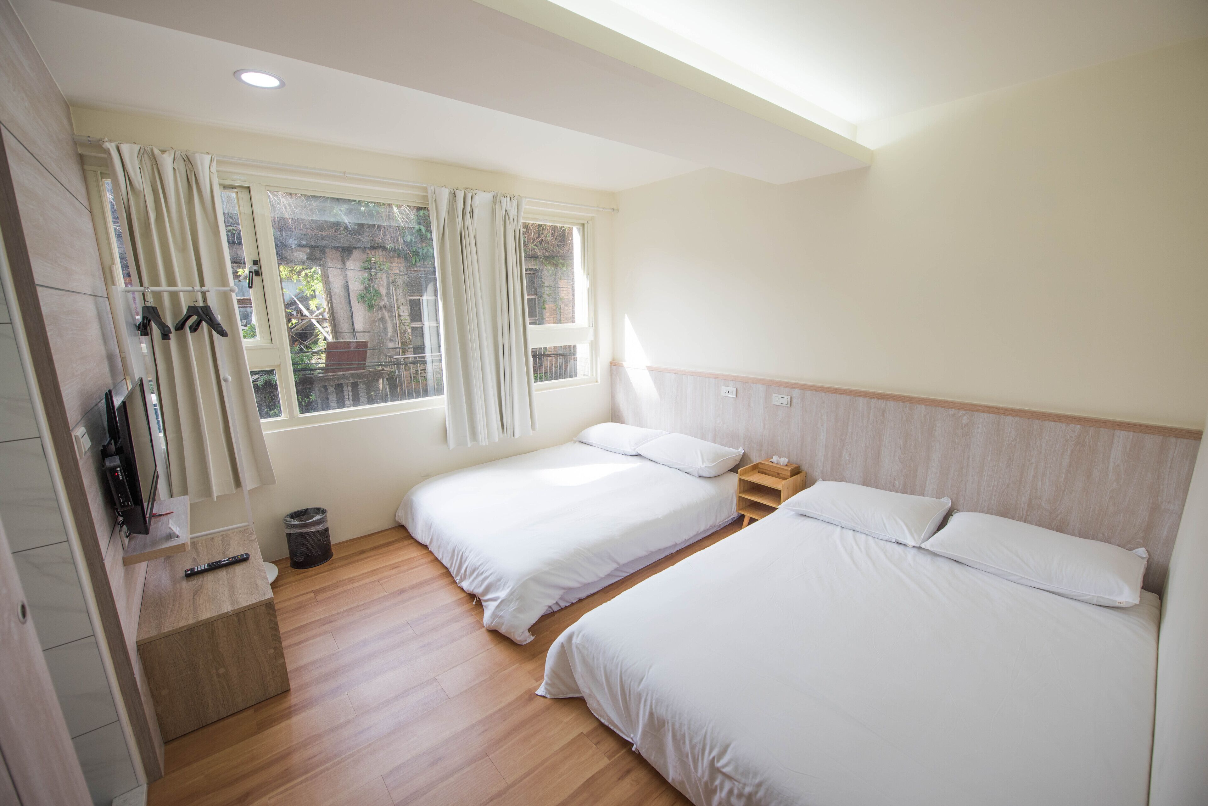 A bedroom with two beds, a TV, and a window with curtains. - ManMan House (New Taipei City)