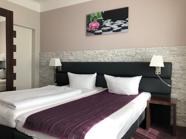 A hotel room with a bed, two bedside lamps, a stone wall, and a painting of flowers and stones. - Hotel Restaurant Sonnenhof (Westerstede)