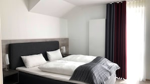 Quarto de hotel moderno com uma cama grande, cabeceira escura e uma mesa de cabeceira com abajur.