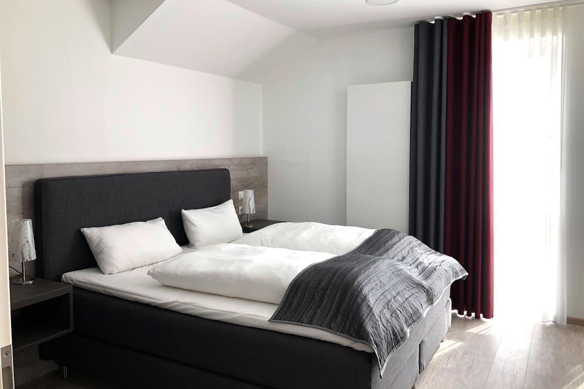 A modern hotel room with a large bed, dark headboard, and a nightstand with a lamp.