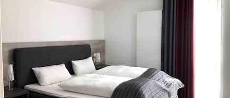 Una habitación de hotel moderna con una cama grande, cabecera oscura y una mesita de noche con lámpara.