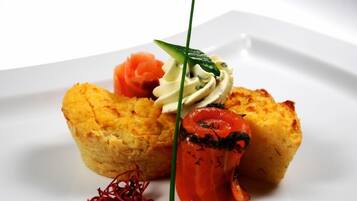 Une assiette blanche contenant une pâtisserie, un morceau de saumon et une cuillerée de crème.