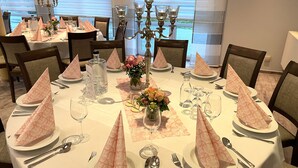 Mesa de jantar posta para uma refeição formal, com toalhas brancas, guardanapos cor-de-rosa e um arranjo de flores como peça central.