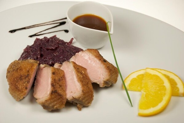 A plate with sliced meat, a small bowl of sauce, and lemon slices.
