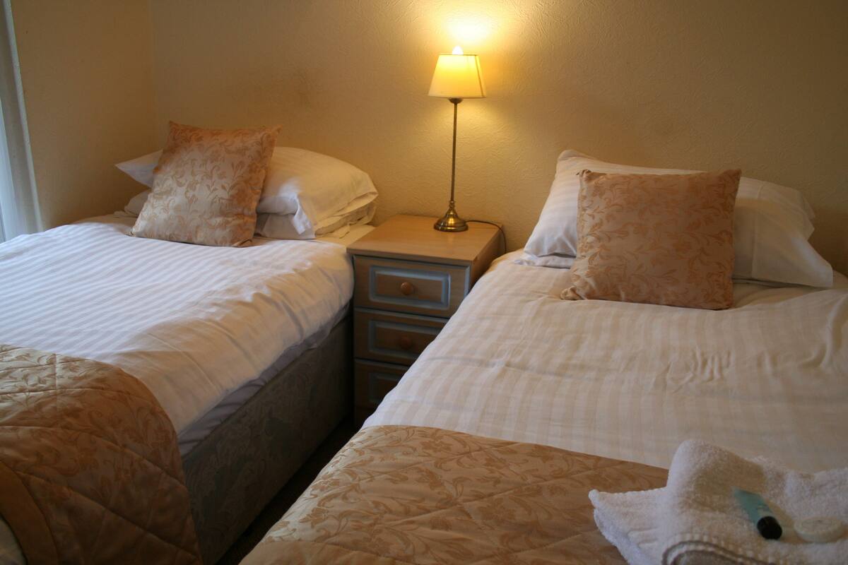 A hotel room with two beds, a nightstand with a lamp, and a small drawer unit.