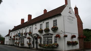Un bâtiment traditionnel de couleur blanche, doté de nombreuses fenêtres et de jardinières, portant l’inscription « Angel Inn ».