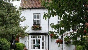 A white building with a tiled roof, a window with a flower box, and outdoor seating with metal chairs and tables. - The Angel Inn (Worksop)