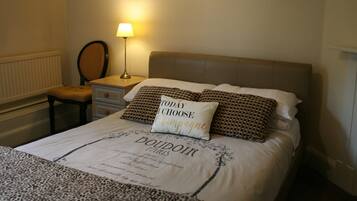 A neatly made bed with a pillow stating "TODAY I CHOOSE Champagne," a lamp, a chair, and a dresser.