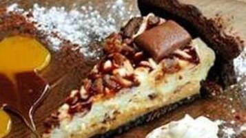 Ein Dessert mit Schokoladenboden, Nüssen und Karamellsoße, serviert auf einem Holztisch.
