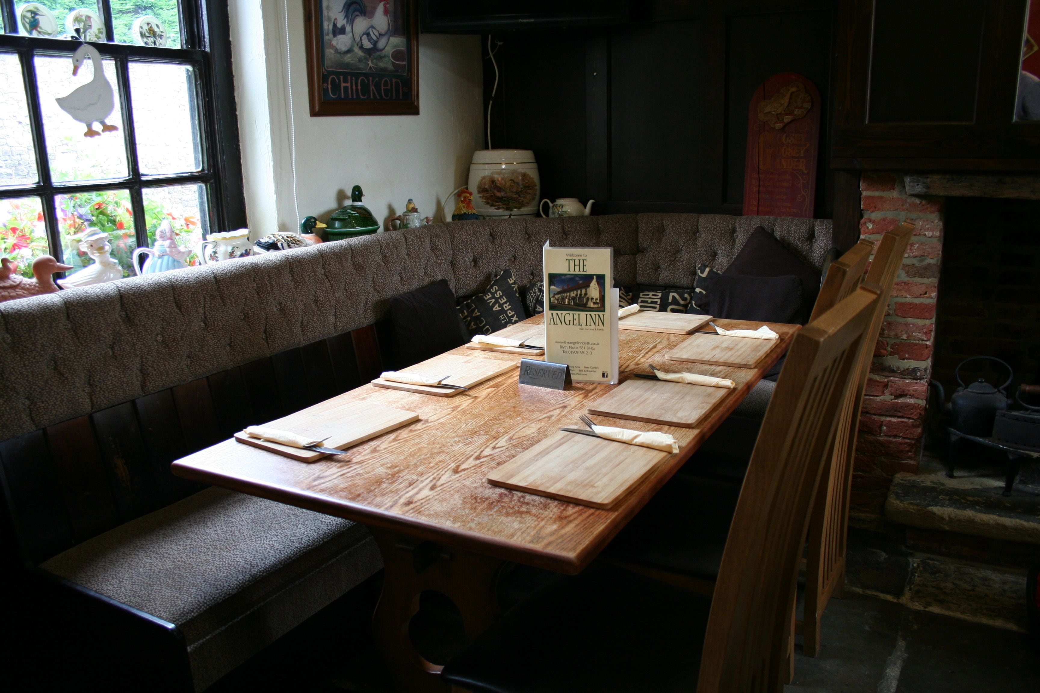 A long wooden table with multiple cutting boards and utensils, set in a cozy room with a brick wall and a window with decorative items.