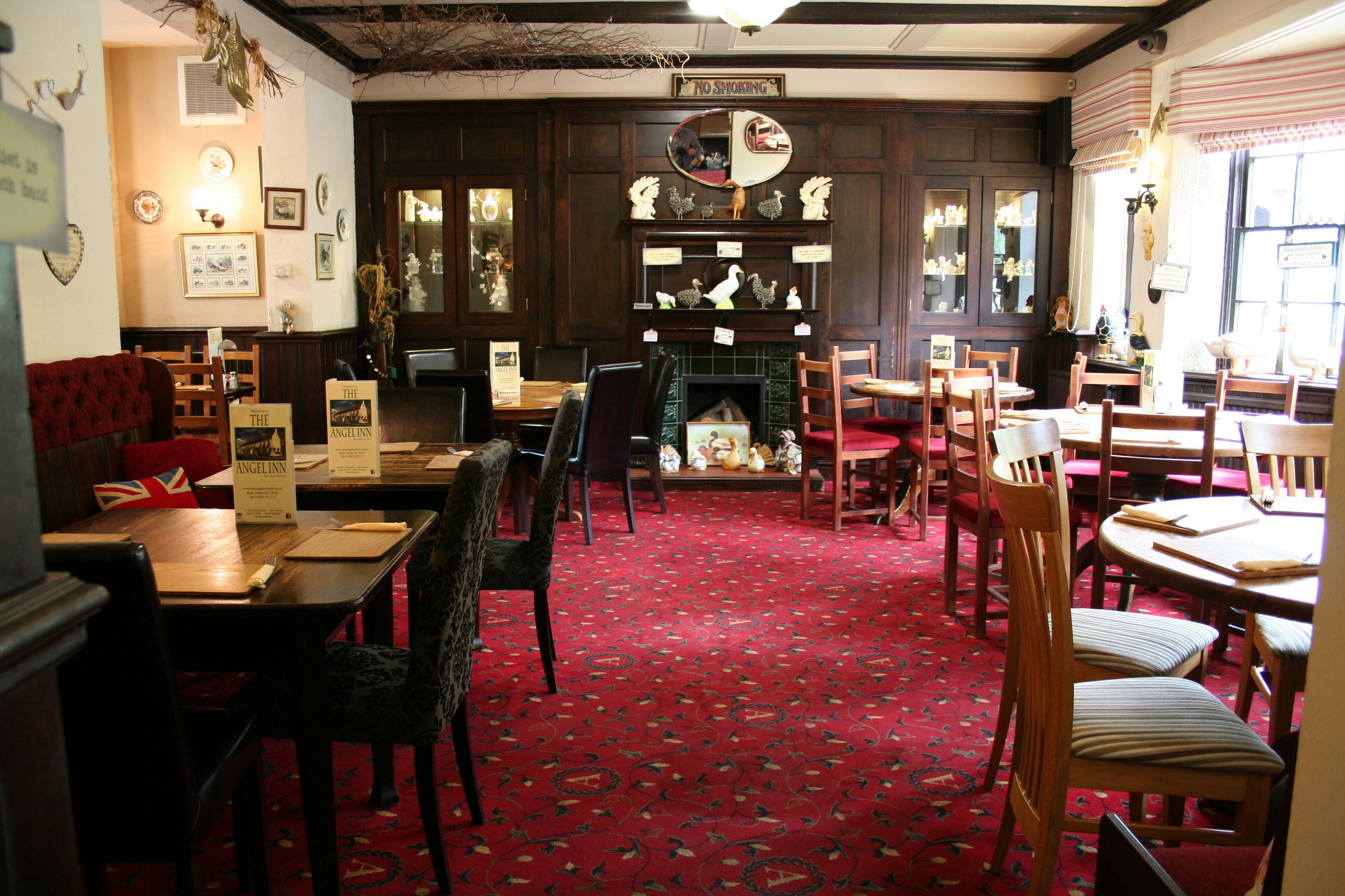A traditional pub interior with wooden furniture, a red carpet, and a fireplace.