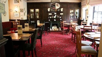 A traditional pub interior with wooden furniture, a red carpet, and a fireplace.