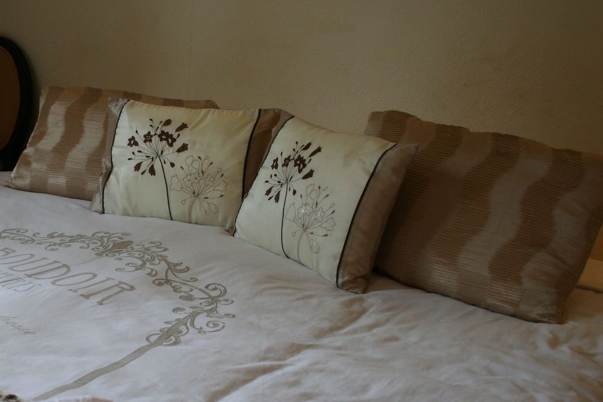 A bed with a floral-patterned bedspread and pillows, a leopard print throw blanket, and a mirror on the wall.