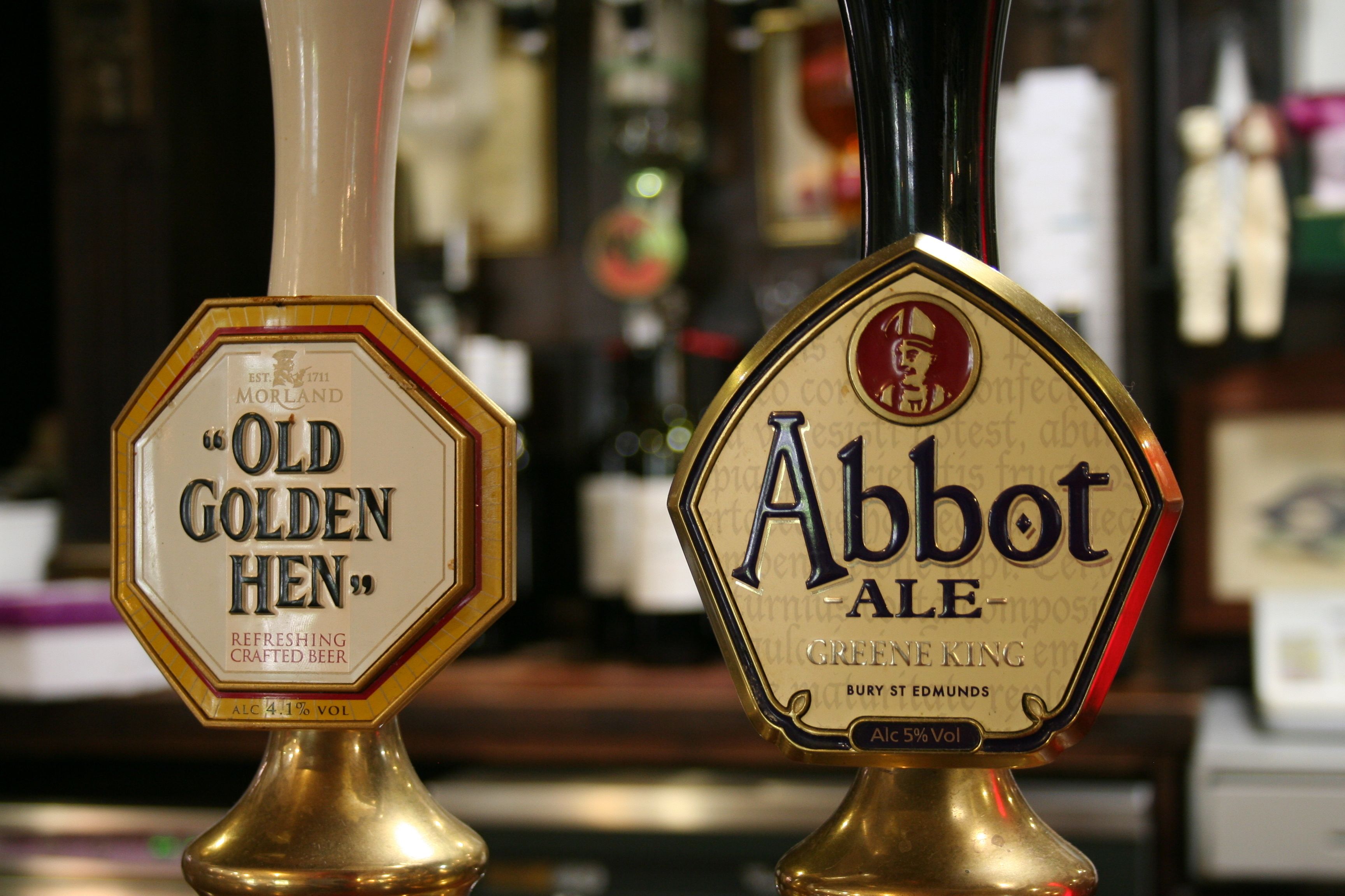 Two beer taps labeled "Old Golden Hen" and "Abbot Ale" with their respective brands and alcohol content.