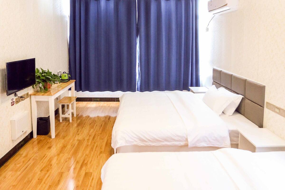 Habitación de hotel con dos camas, un escritorio con televisor y una ventana grande con cortinas.