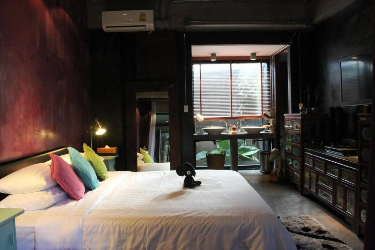 A bedroom with a bed, pillows, a small statue, a window, and a dresser.