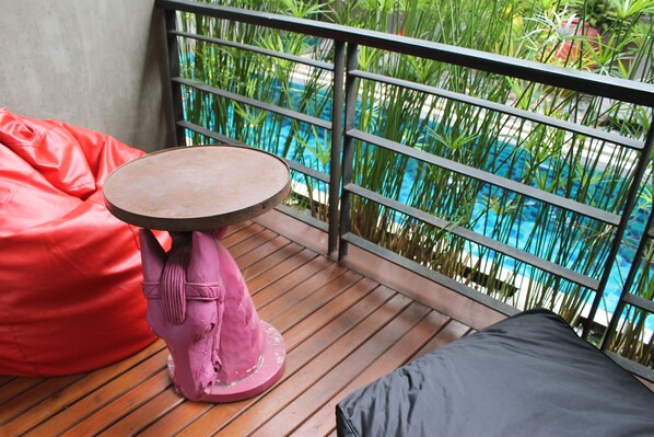A balcony with a wooden floor, a round table, a pink horse sculpture, and a red bean bag. - Villa Thapae Chiang Mai (Chiang Mai)