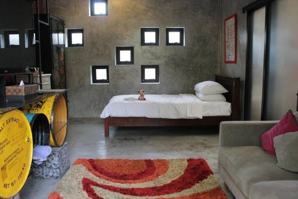 A bedroom with a bed, a sofa, a small table, and a yellow barrel.