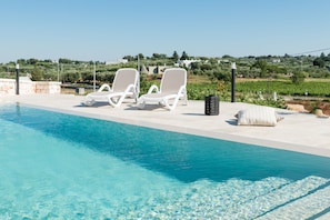 A swimming pool with two lounge chairs and a small table, surrounded by a stone wall and a view of a green landscape. - Villa d'Itria with Trullo by Wonderful Italy (Ostuni)