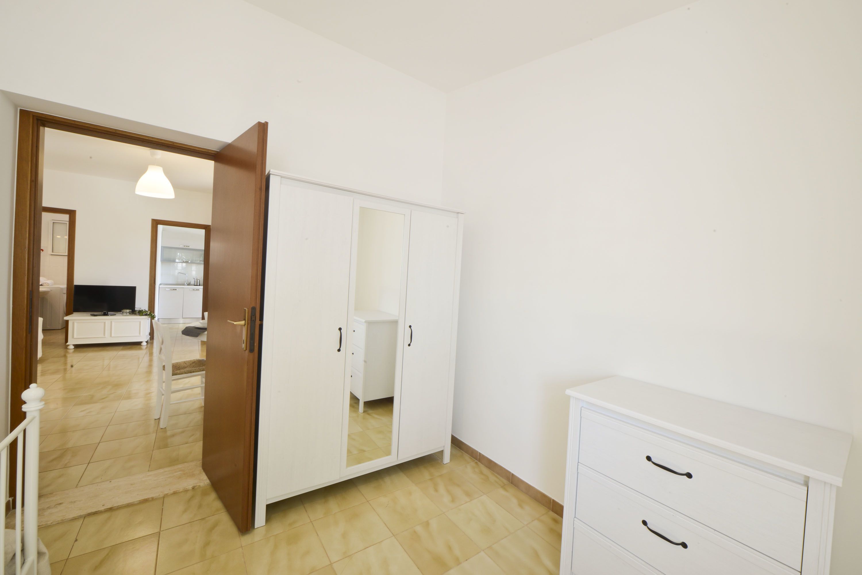 Een kamer met een kast, een klein meubeltje en een televisie op de achtergrond.
