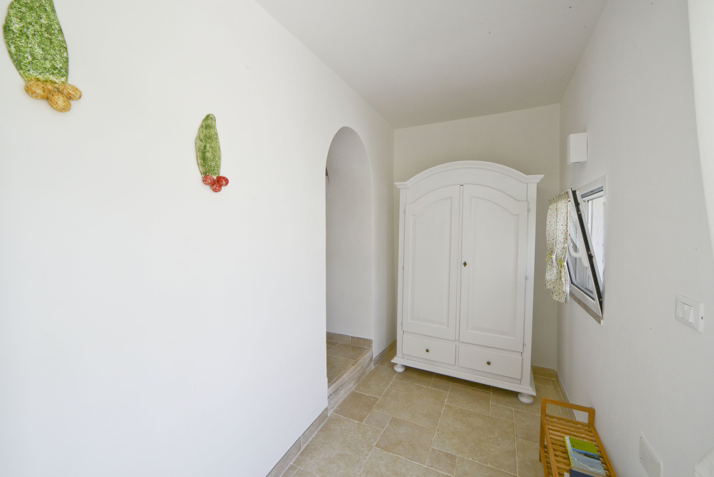 Un couloir avec une porte en arc blanc, une armoire blanche et un petit banc en bois sur lequel sont posés des livres.