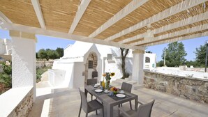 An outdoor patio with a table set for four, surrounded by stone walls and a white building in the background. - Villa d'Itria with Trullo by Wonderful Italy (Ostuni)