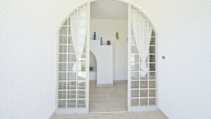 A white arched doorway leading to a room with a white counter and a small shelf with decorative items. - Villa d'Itria with Trullo by Wonderful Italy (Ostuni)