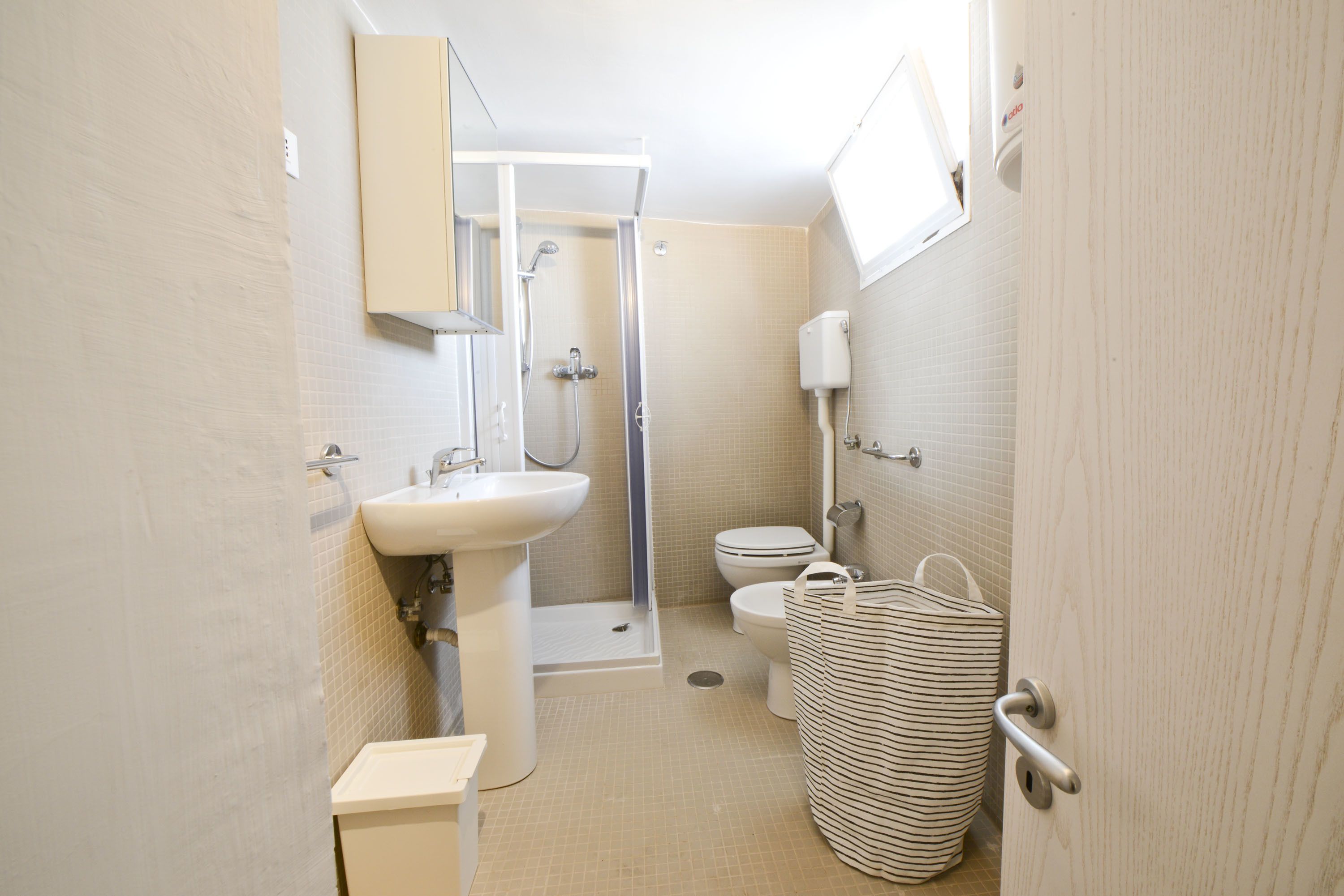 A compact bathroom with a sink, toilet, shower, and a striped bag.