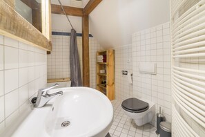 Un baño con un lavabo blanco, un inodoro y un estante de madera con toallas.