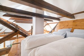 Un dormitorio con techo inclinado, vigas de madera y cama con ropa de cama blanca.