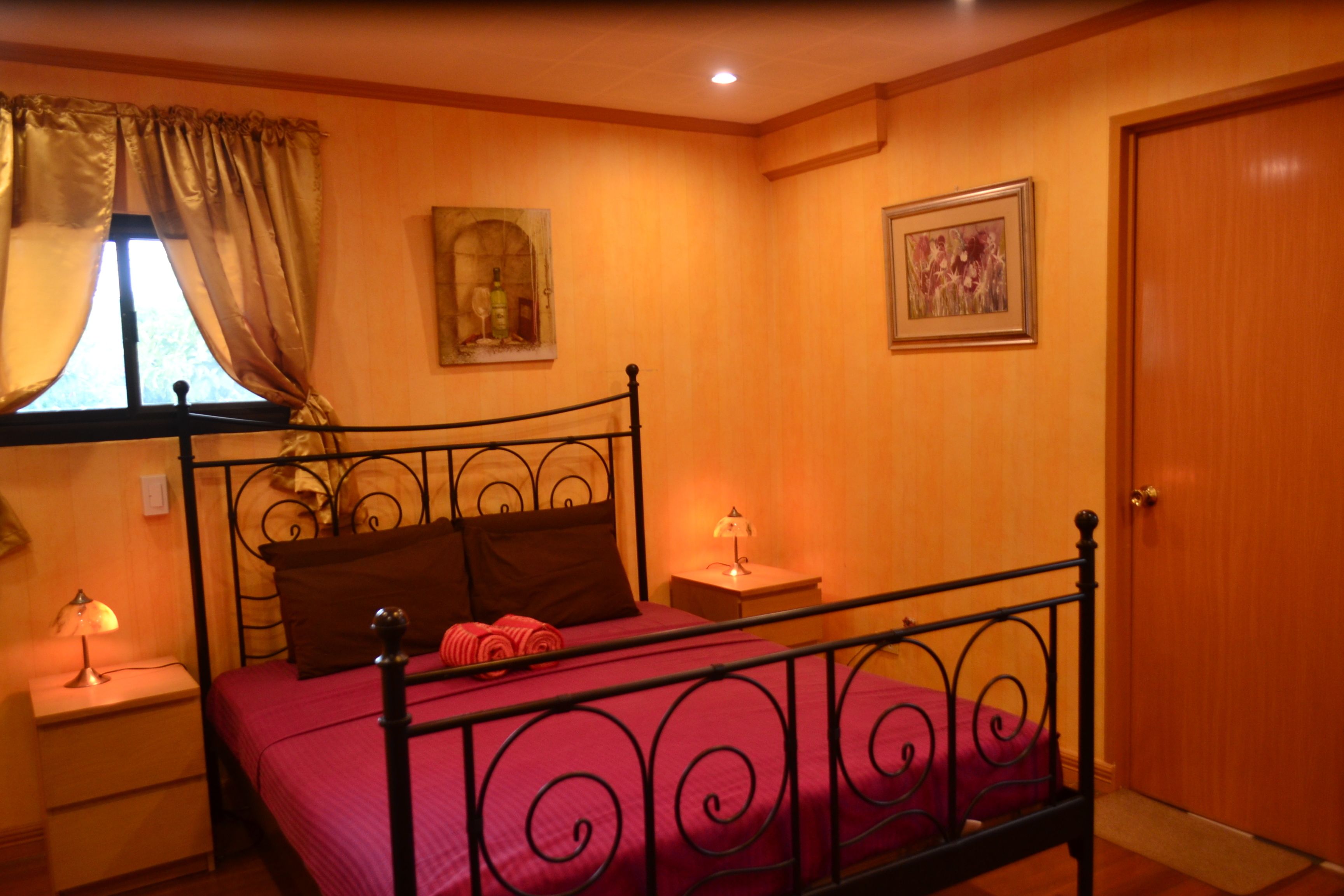 A bedroom with a metal bed frame, a red bedspread, and two nightstands with lamps.