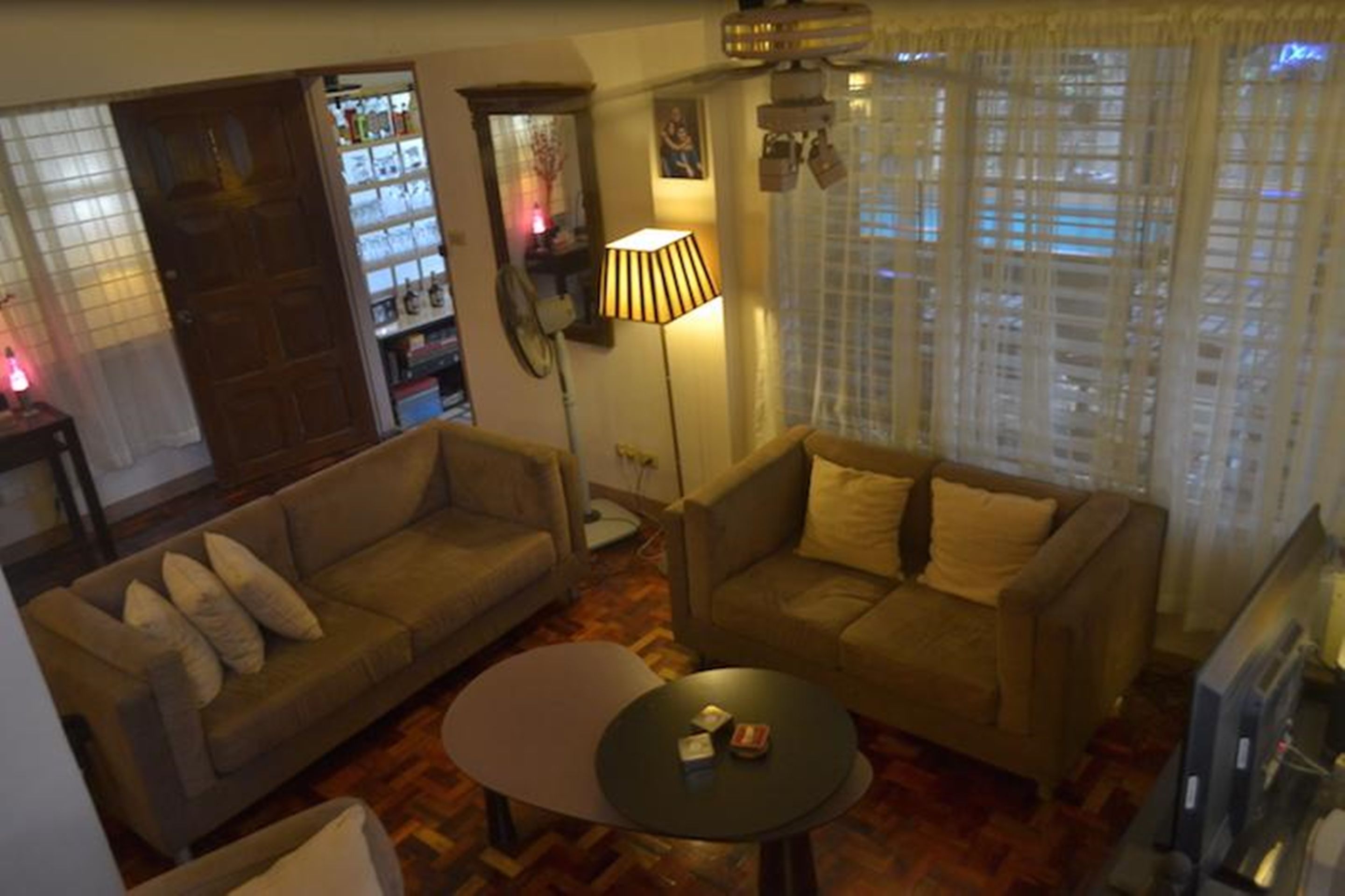 A living room with two sofas, a coffee table, and a lamp. There is a door leading to a kitchen area with a refrigerator and a window with curtains.
