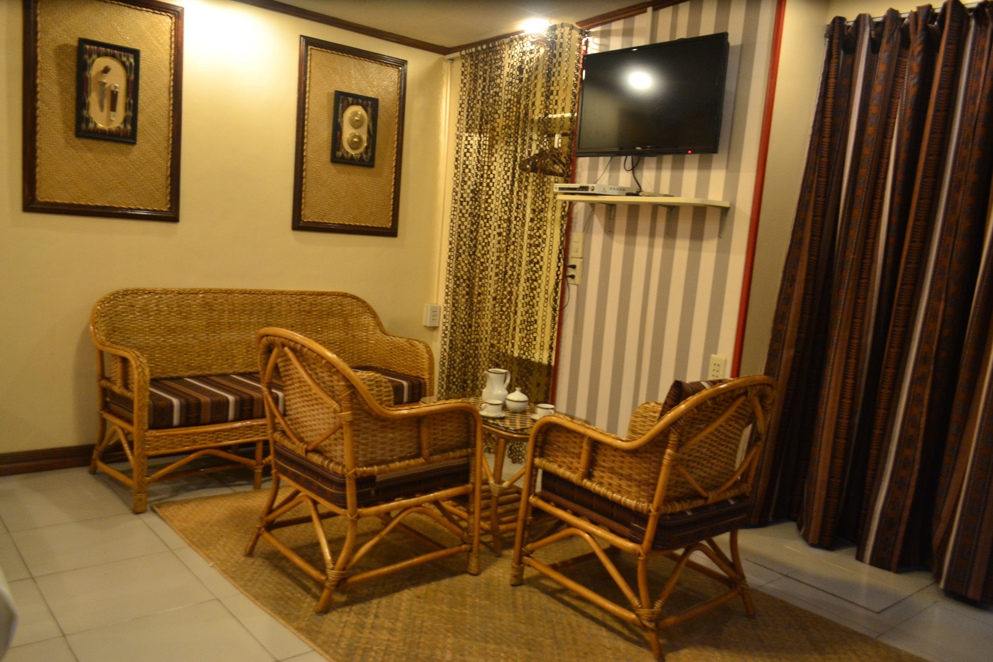 A living room with wicker furniture, a television mounted on the wall, and striped curtains.