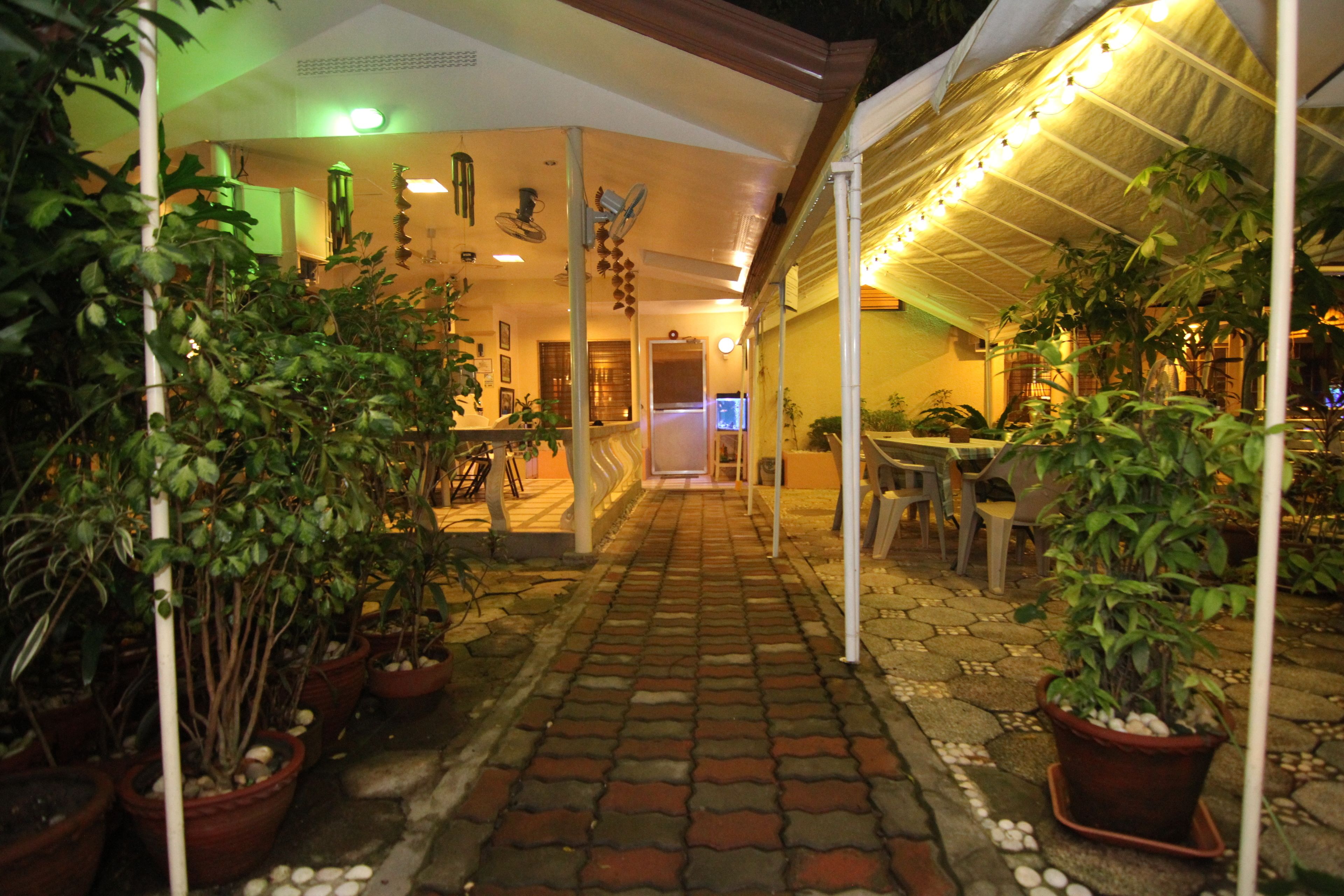 A covered outdoor area with potted plants, a brick pathway, and a seating area.