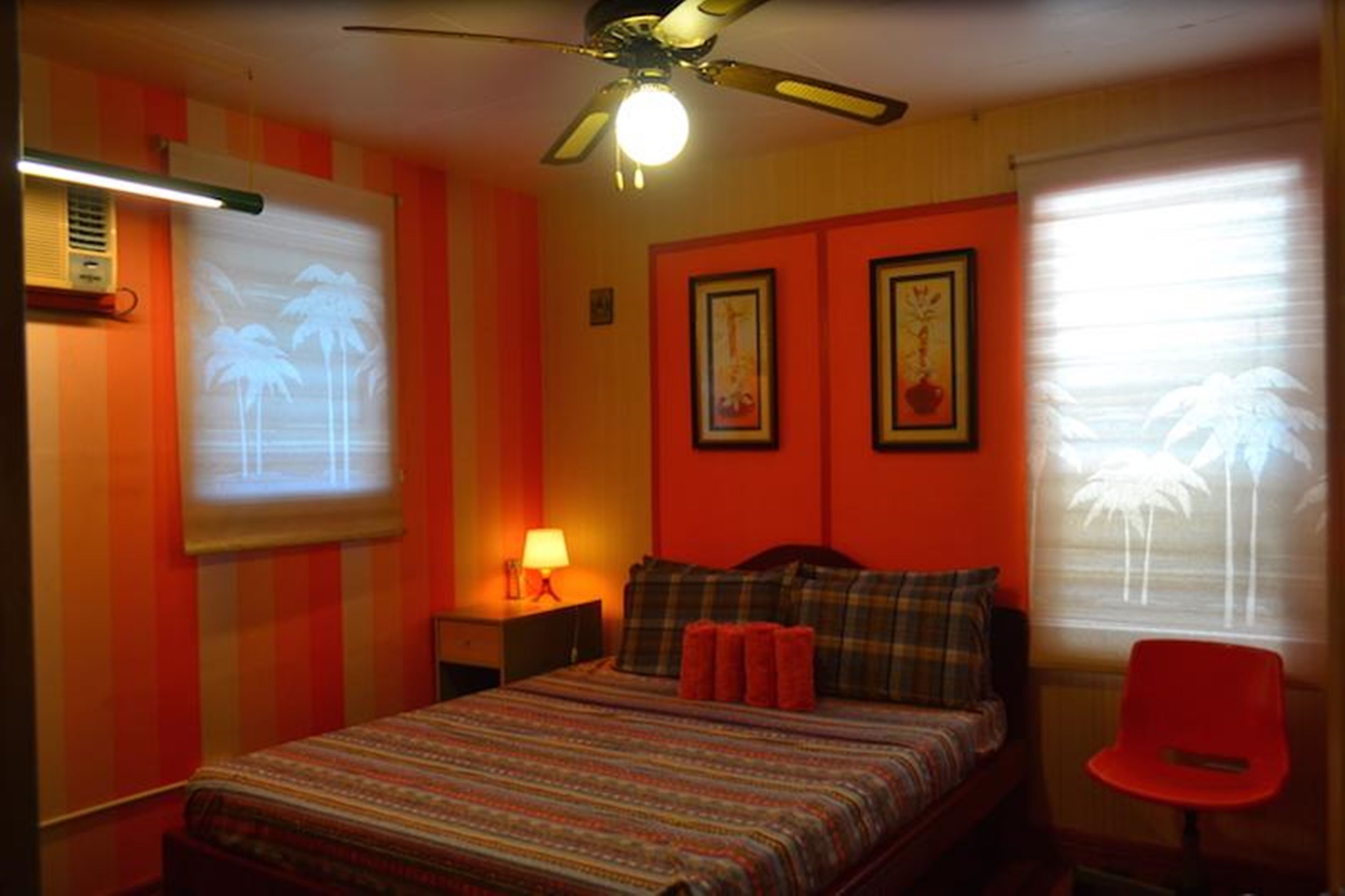 A bedroom with a bed, a nightstand, a red chair, and a ceiling fan.