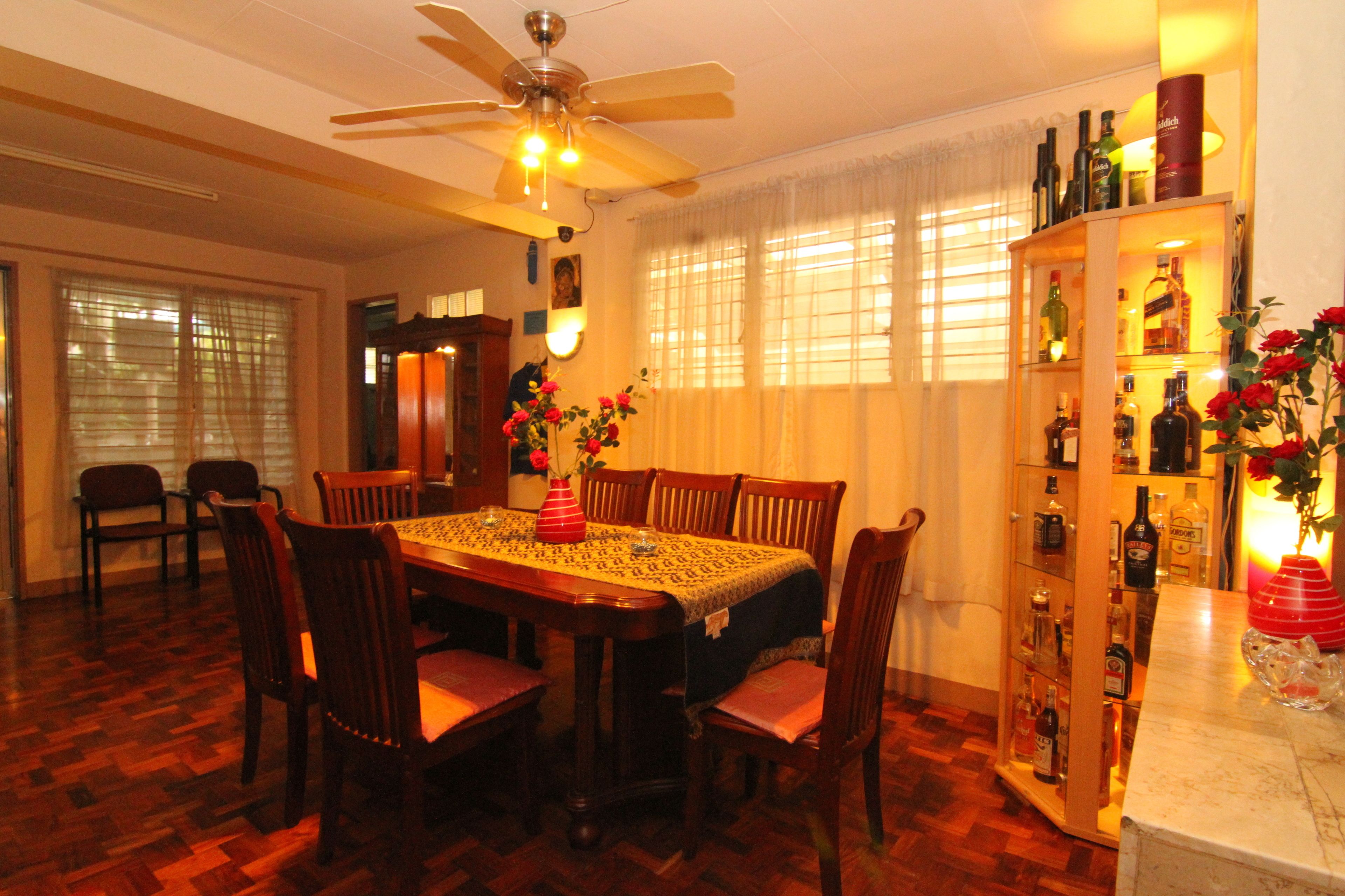Un coin repas avec une table et des chaises en bois, un ventilateur de plafond et un meuble à vin contenant des bouteilles.
