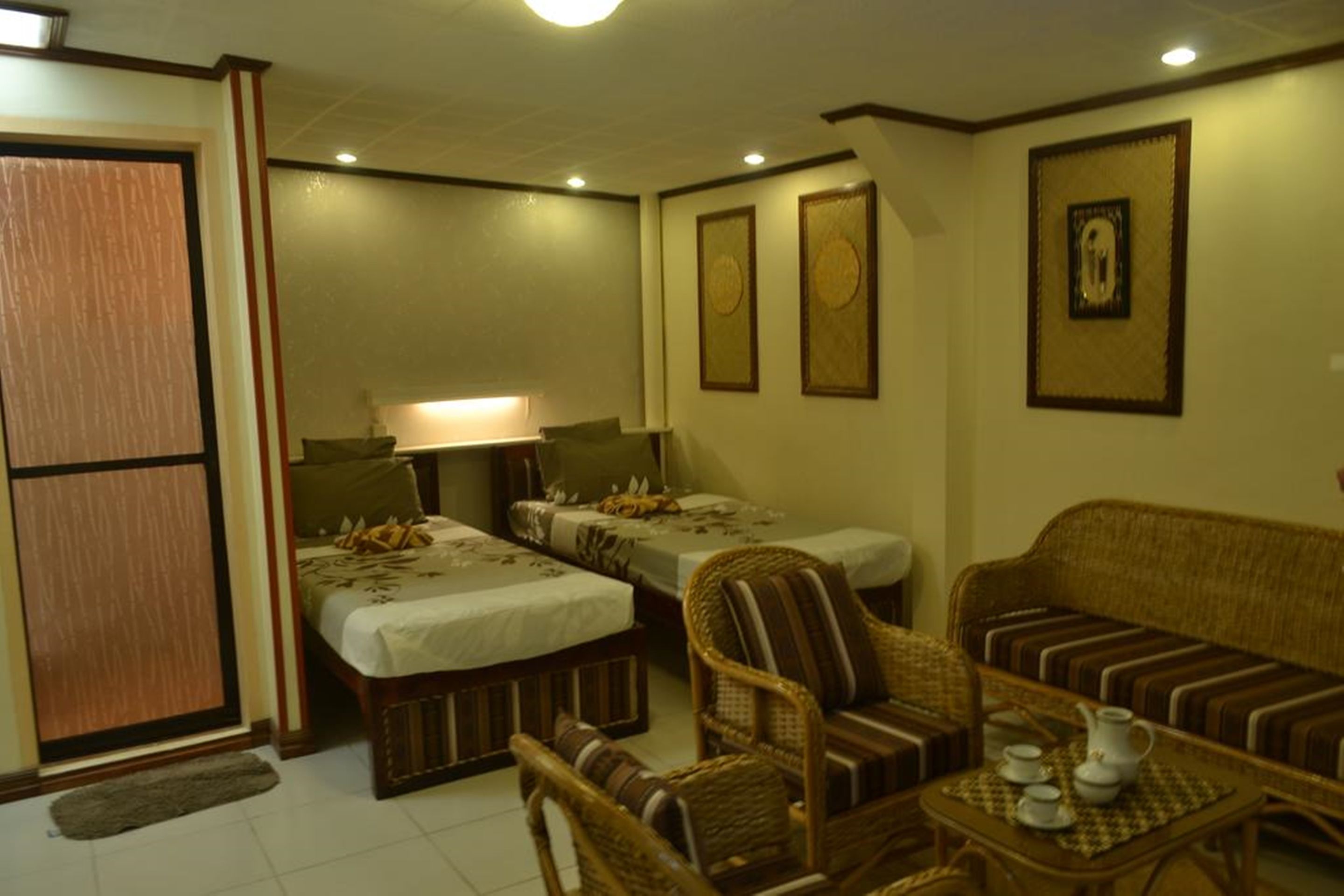 Une chambre avec deux lits simples, un canapé, une petite table avec une théière et des tableaux encadrés aux murs.