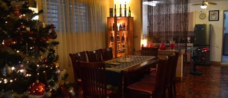 A dining area with a Christmas tree, a wooden cabinet with bottles, and a dining table.