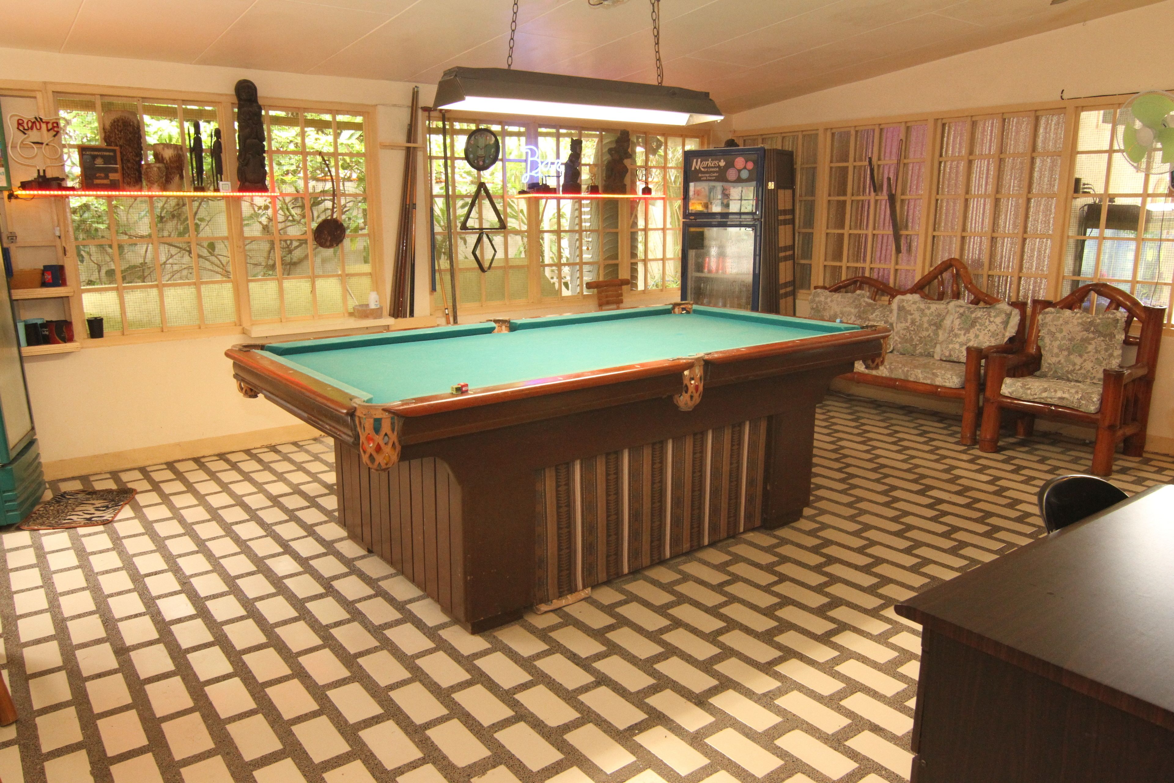 A pool table in a room with patterned flooring, a bar area, and a seating area with chairs.