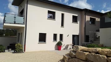 A modern two-story building with a balcony, multiple windows, and a stone staircase leading to the entrance.