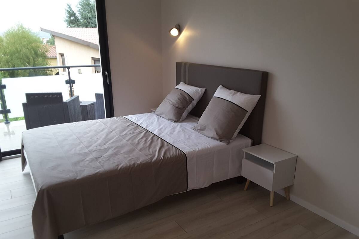 A modern bedroom with a large bed, a nightstand, and a view of the outdoors.