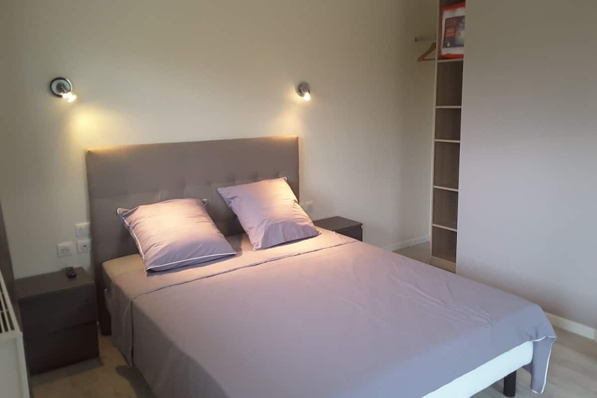 A neatly made bed with a headboard, two bedside tables, and a wall-mounted shelf.