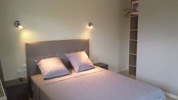 A neatly made bed with a headboard, two bedside tables, and a wall-mounted shelf.