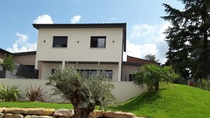 Una casa moderna de dos pisos con un jardín bien cuidado, que incluye un bonsái y un muro de piedra.