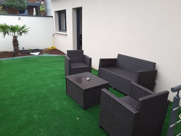 Un patio con mobiliario de mimbre, incluyendo un sofá y dos sillones, junto con una mesita.