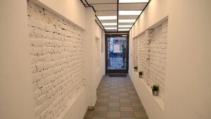 A narrow hallway with white brick walls, a tiled floor, and a ceiling with recessed lighting.