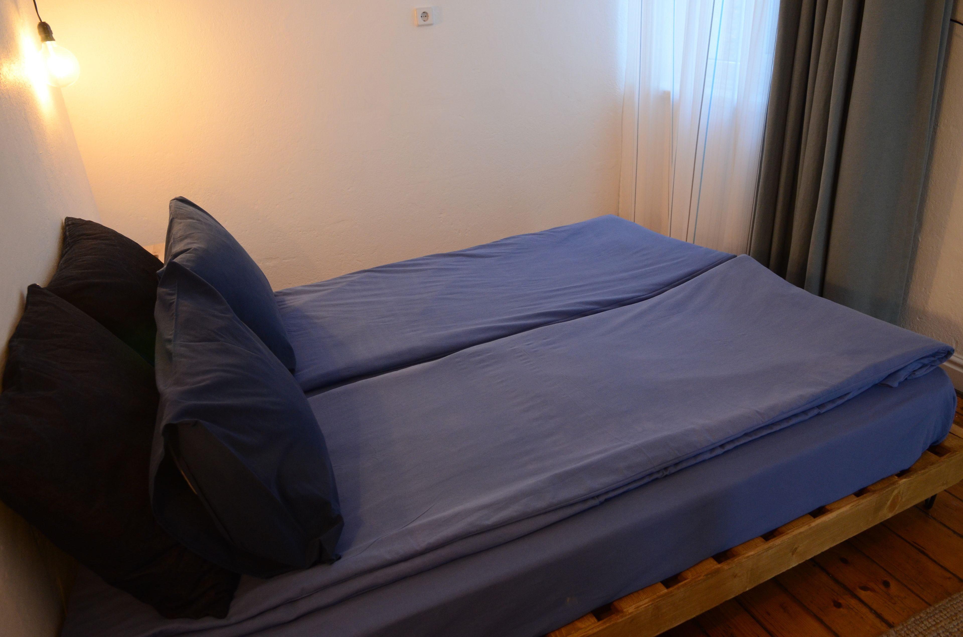 A single bed with blue bedding in a room with wooden flooring and a white wall.