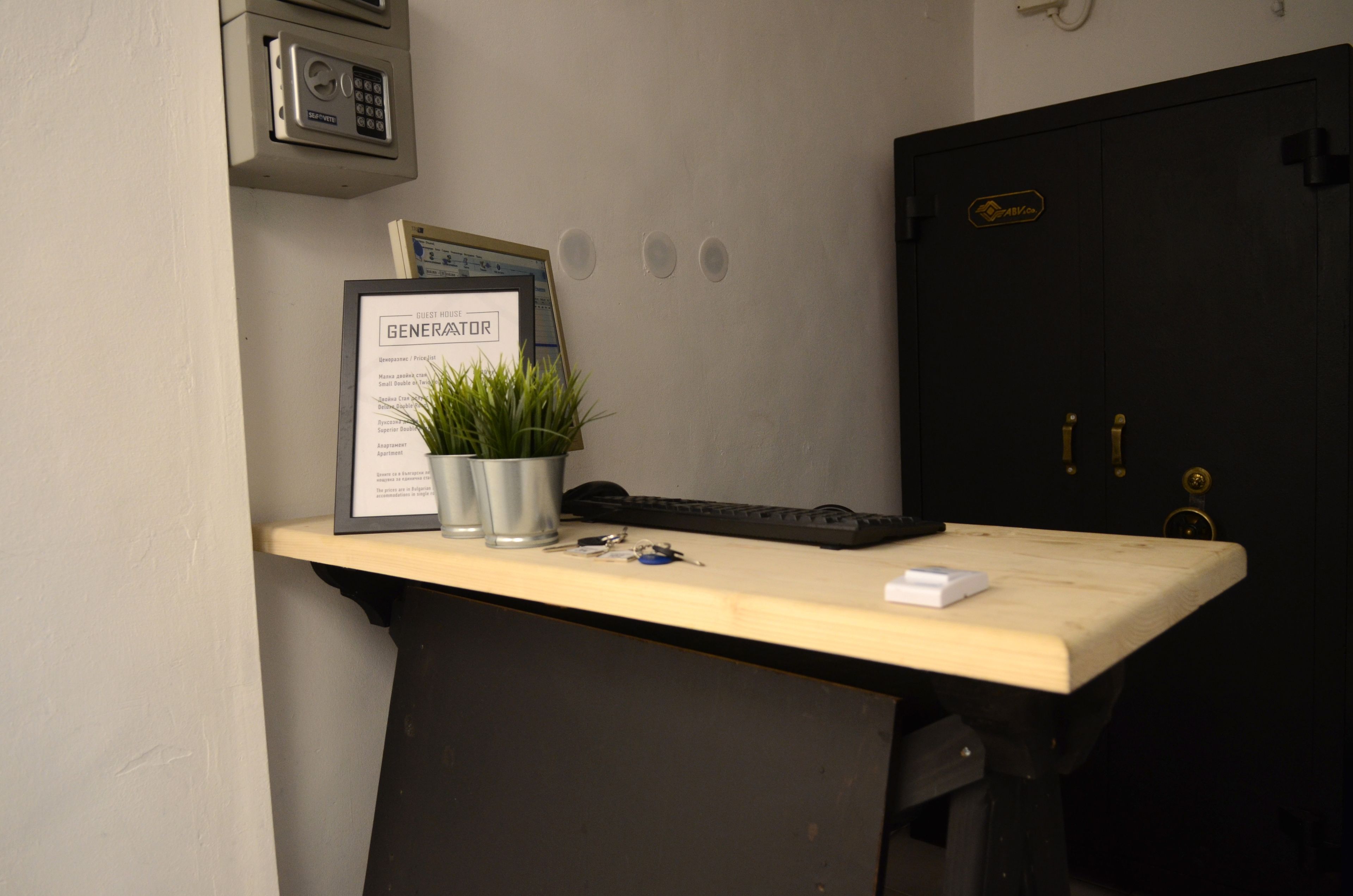 Una mesa de recepción con un letrero enmarcado, una planta en maceta, un teclado y un pequeño objeto blanco.
