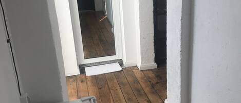 A narrow hallway with wooden flooring, white walls, and a white refrigerator in the foreground.