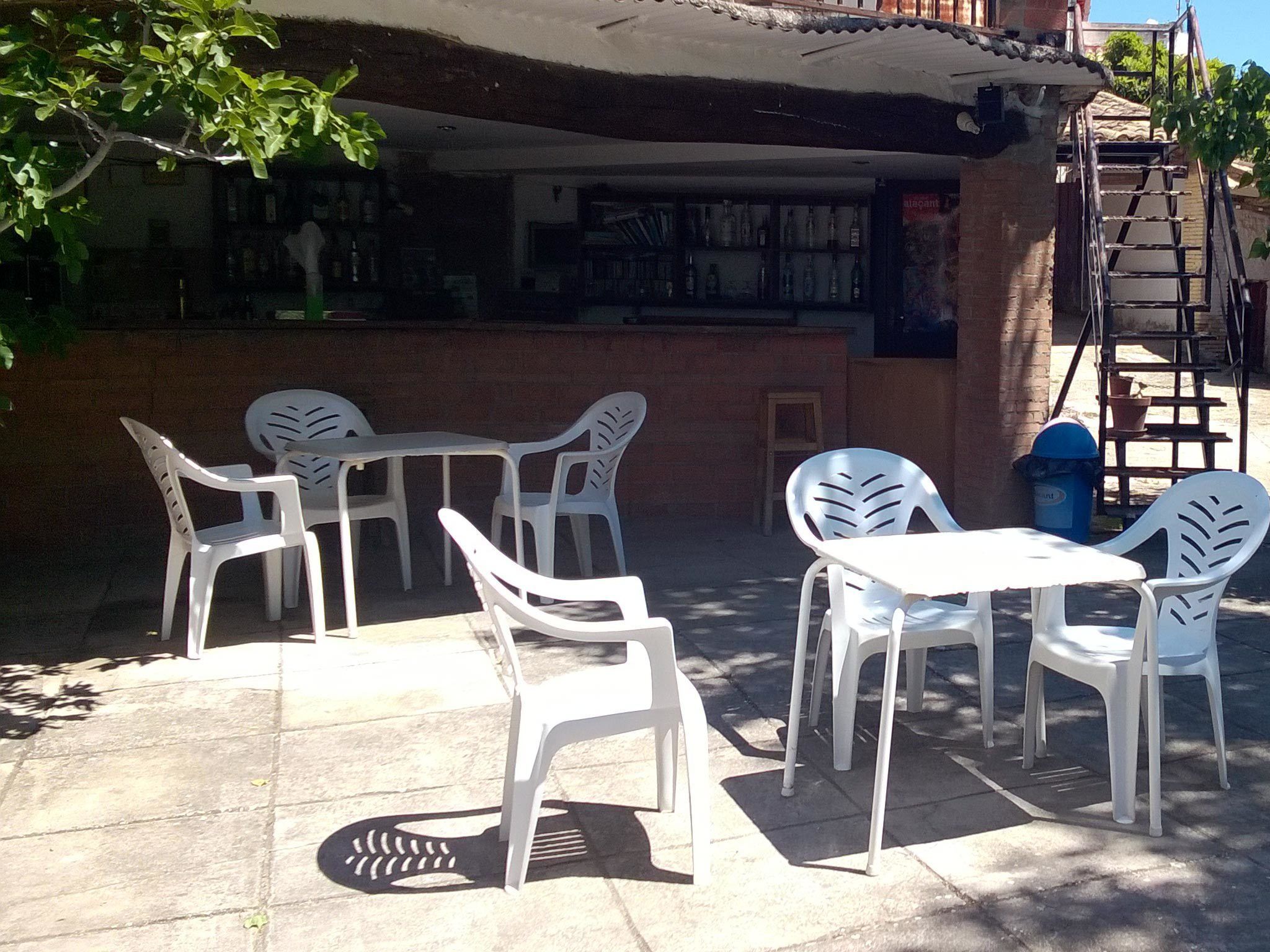 Outdoor seating with white plastic chairs and tables, a brick wall, and a ladder leading to an upper level.